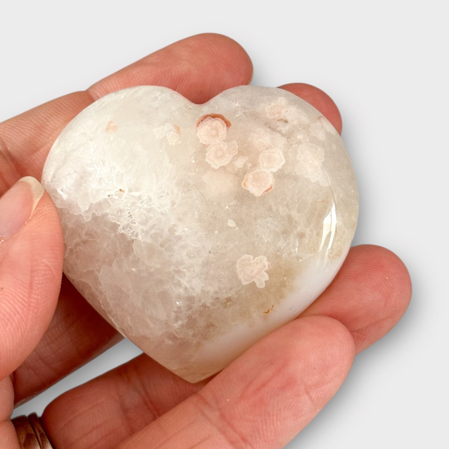 A Flower Agate Heart resting in the palm of a hand, highlighting its compact size, soft floral patterns, and polished heart shape.