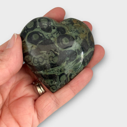 A polished Kambaba Jasper Heart resting in the palm of a hand, highlighting its compact size, natural swirls, and glossy texture.