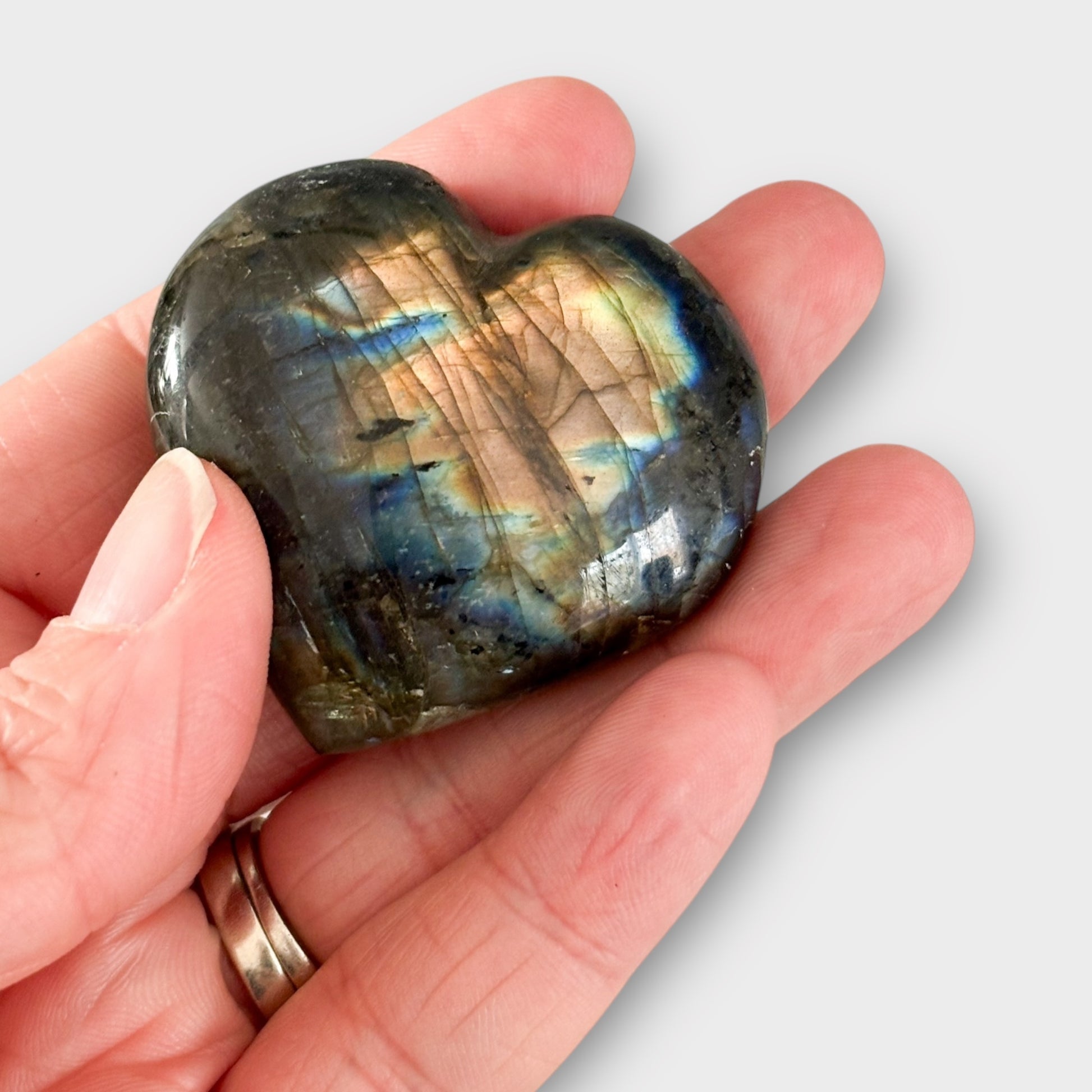 A Labradorite Heart cradled in the palm of a hand, showing its compact size and stunning flashes of blue and green hues.