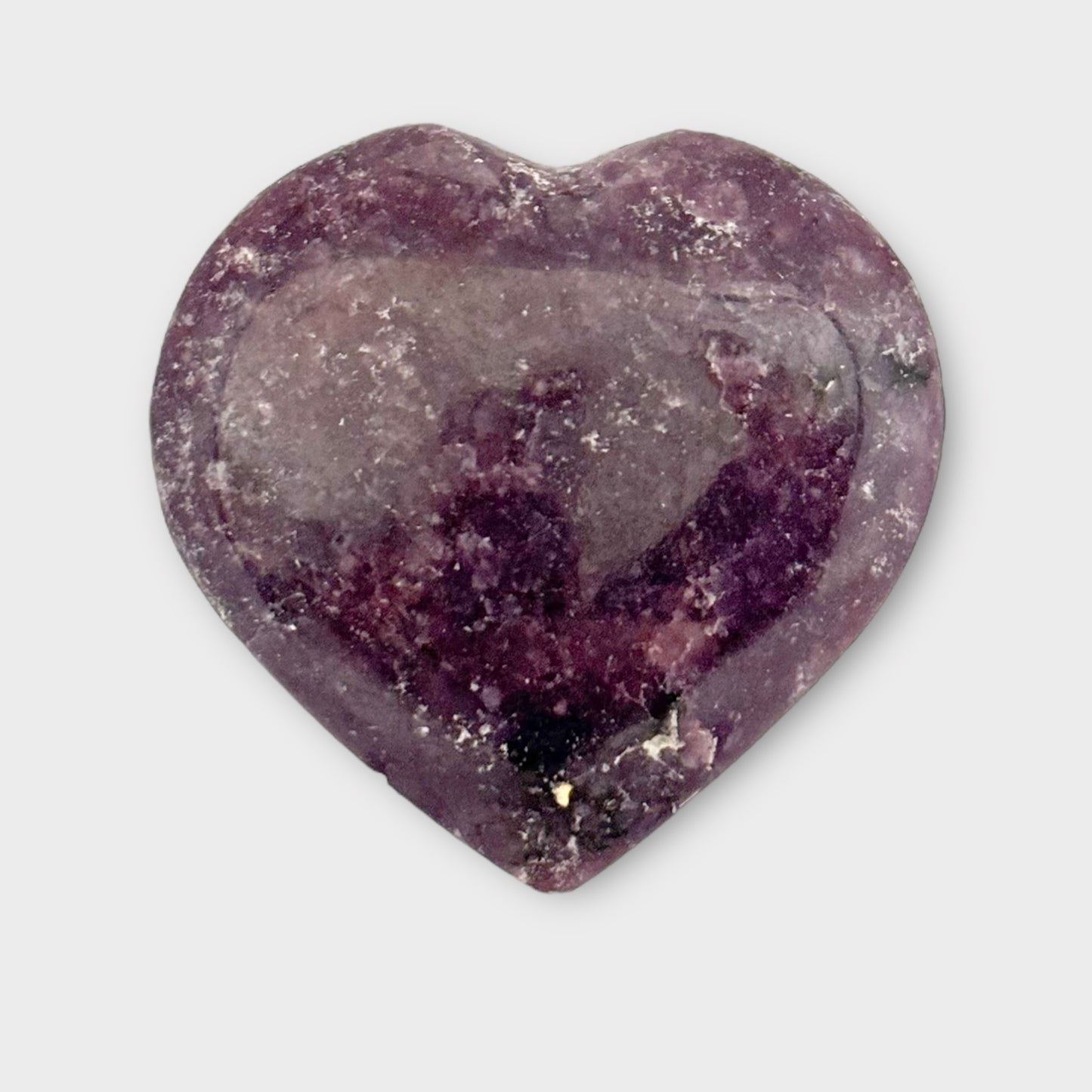 Close-up of a Lepidolite Heart resting on a plain white background, showcasing its natural stone patterns and calming hues