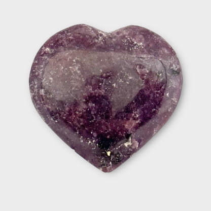 Close-up of a Lepidolite Heart resting on a plain white background, showcasing its natural stone patterns and calming hues