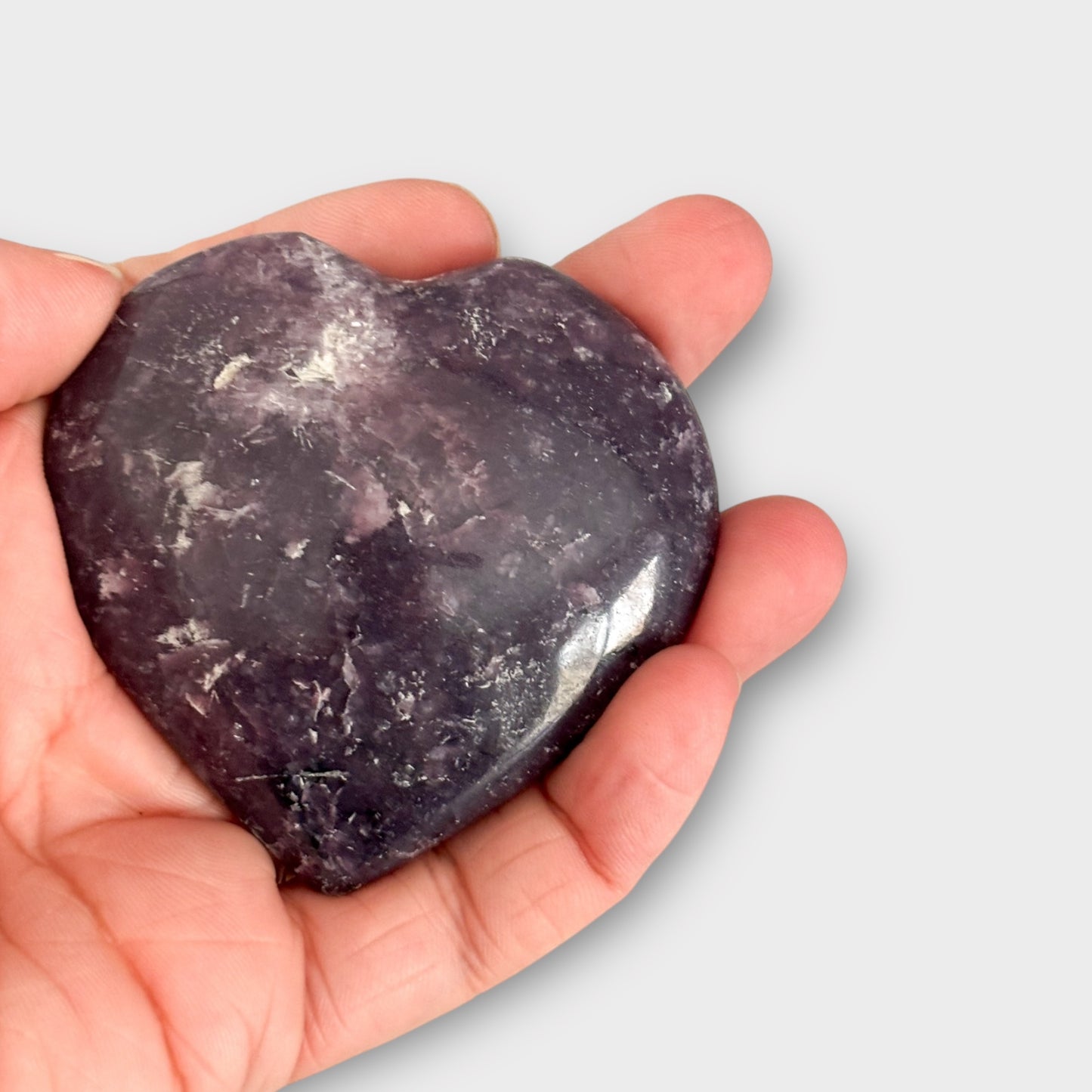 A Lepidolite Heart held in the palm of a hand, demonstrating its palm-sized shape and portability for everyday use.