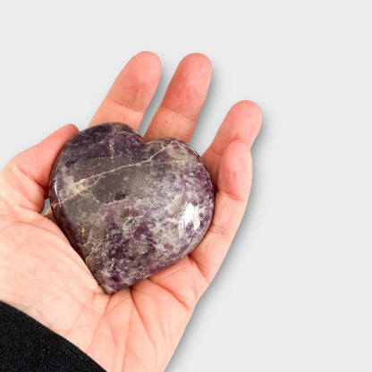 A Lepidolite Heart held gently in the palm of a hand, demonstrating its palm-sized shape and comforting energy.