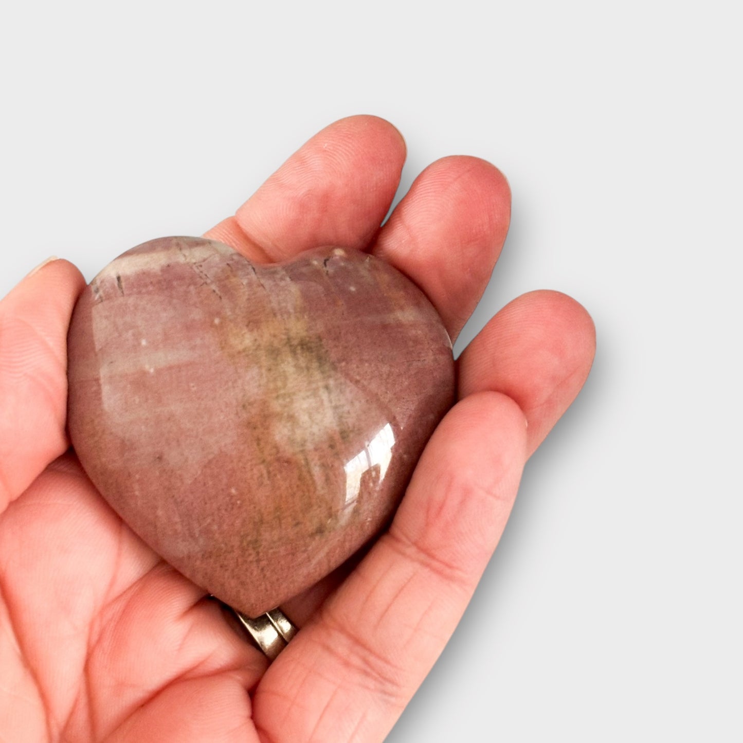 A pink Polychrome Jasper Heart resting in the palm of a hand, highlighting its compact size, vibrant color, and polished finish.