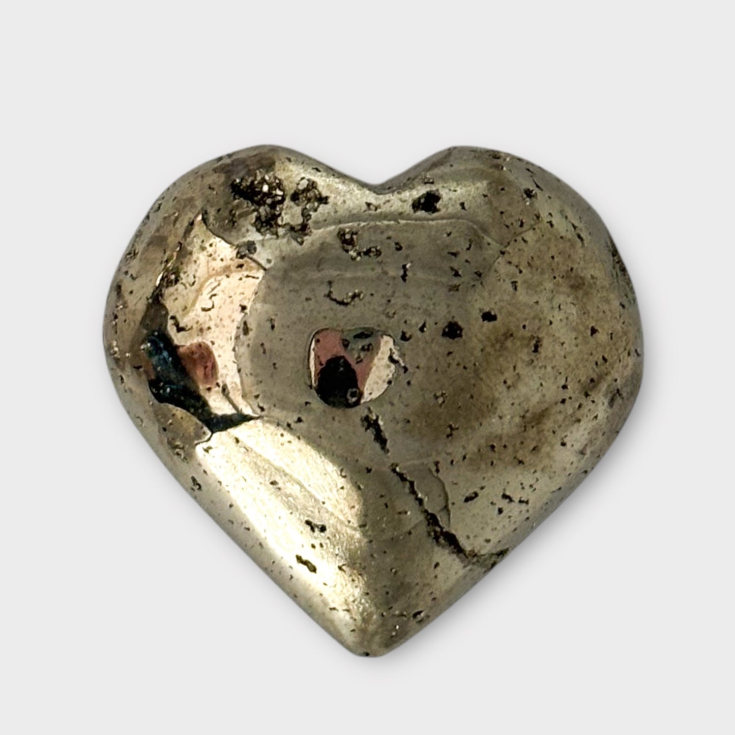 A polished Pyrite Heart resting on a white background, capturing its radiant golden hues and heart shape.